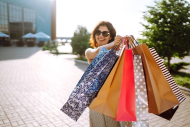 Alışveriş zamanı. Alışveriş merkezinin yakınında alışveriş torbaları taşıyan genç bir kadın. Tüketim, satış, alım satım, alışveriş, yaşam tarzı konsepti. Yaz.