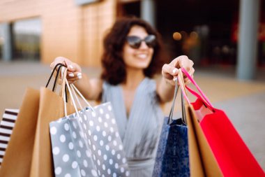 Alışveriş zamanı. Alışveriş merkezinin yakınında alışveriş torbaları taşıyan genç bir kadın. Tüketim, satış, alım satım, alışveriş, yaşam tarzı konsepti. Yaz.