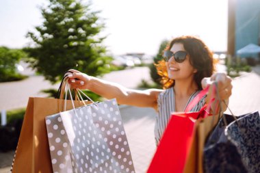 Alışveriş zamanı. Alışveriş merkezinin yakınında alışveriş torbaları taşıyan genç bir kadın. Tüketim, satış, alım satım, alışveriş, yaşam tarzı konsepti. Yaz.