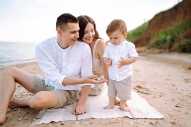 Baba, anne ve çocuk sahilde dinleniyor. Genç aile yaz tatilinde eğleniyor. Seyahat, doğa, aktif yaşam tarzı, tatil köyü kavramı.