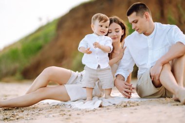 Baba, anne ve çocuk sahilde dinleniyor. Genç aile yaz tatilinde eğleniyor. Seyahat, doğa, aktif yaşam tarzı, tatil köyü kavramı.