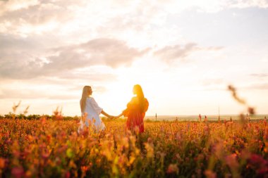Portrait of two young woman in stylish dress posing in the blooming field. Nature, vacation, relax and lifestyle. Fashion concept.