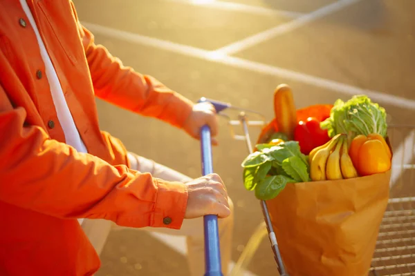 Healthy vegan vegetarian food in a paper bag  in the male hands. Young man with shopping bag near the car. Consumerism, sale, purchases, shopping, lifestyle concept.