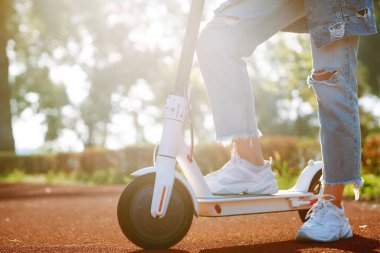 Gün batımında elektrikli scooter kullanan bir kadın, yakın plan. Ekolojik ulaşım kavramı.