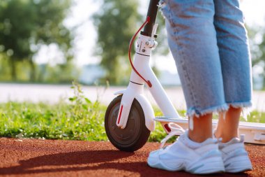 Gün batımında elektrikli scooter kullanan bir kadın, yakın plan. Ekolojik ulaşım kavramı.