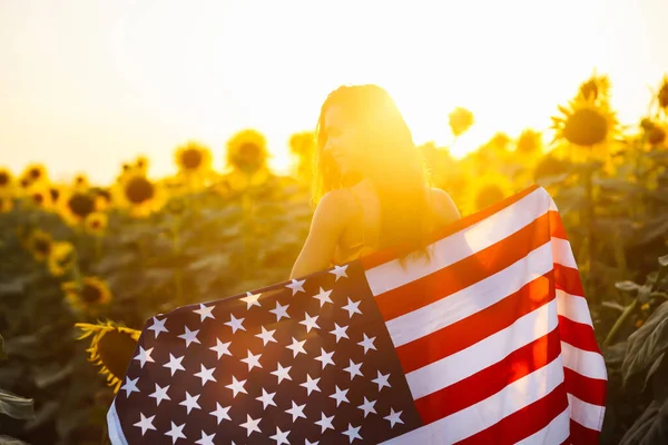年轻女子自豪地在向日葵地里挥舞着美国国旗 爱国者日落时升起美国国旗 独立日 7月4日 — 图库照片