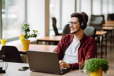 Genç adam ofisteki bir bilgisayarda çalışıyor. Dizüstü bilgisayardan çalışan serbest çalışan biri. İş, eğitim kavramı.