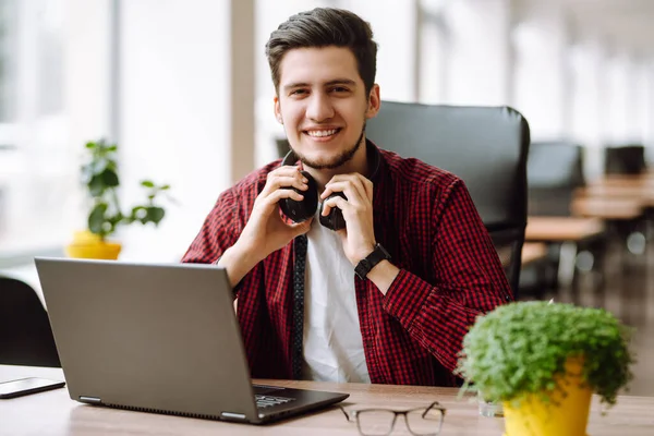 Young man works at a computer in the office. Freelancer working from a laptop. Business, education concept.