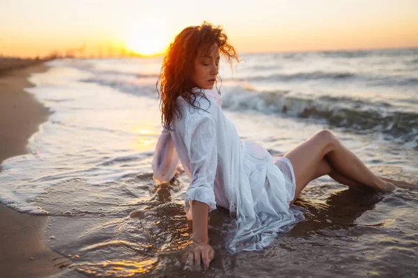 白いなびくドレスを着た若い幸せな女性が海岸沿いを歩いている 少女は不思議な日の出を見る リラックスしてライフスタイルのコンセプト — ストック写真