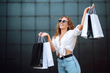 Alışveriş torbalı şık bir kadın şehrin sokaklarında yürüyor. Tüketim, satın alma, alışveriş, yaşam tarzı konsepti.