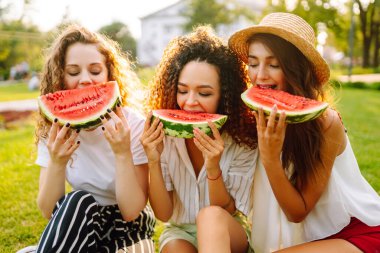 Parkta karpuz yiyen çekici genç kadınlar. İnsanlar, yaşam tarzı, seyahat, doğa ve tatil konsepti. Yaz konsepti.