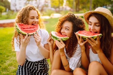 Parkta karpuz yiyen çekici genç kadınlar. İnsanlar, yaşam tarzı, seyahat, doğa ve tatil konsepti. Yaz konsepti.