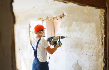 Kasklı bir tamirci ve aletli bir kazan giysisi. Daire tamiri ve yenileme konsepti. İnşaat, çalışma ekipmanları ve insan konsepti