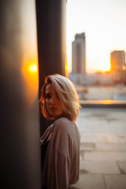 Çatıda poz veren genç bir kadın, çatıdan şehrin muhteşem manzarası. İnsanlar, yaşam tarzı, rahatlama konsepti. Moda, tarz kavramı.