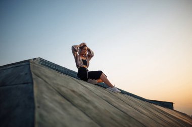 Gün batımında çatıda poz veren genç bir kadın, Özgürlük Şehri atmosferi. İnsanlar, yaşam tarzı, rahatlama konsepti.