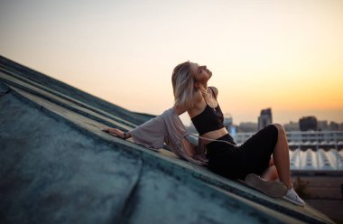 Gün batımında çatıda poz veren genç bir kadın, Özgürlük Şehri atmosferi. İnsanlar, yaşam tarzı, rahatlama konsepti.
