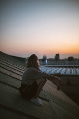 Gün batımında çatıda poz veren genç bir kadın, Özgürlük Şehri atmosferi. İnsanlar, yaşam tarzı, rahatlama konsepti.