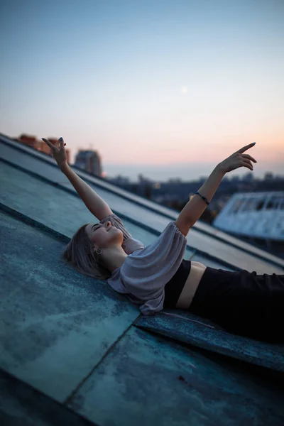 夕暮れ時に屋根の上にポーズを若い女性は 自由都市の雰囲気 ライフスタイル リラクゼーションの概念 — ストック写真