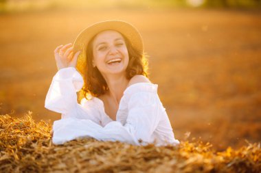 Gün batımında samanlığın yanında mutlu bir kadın. Moda konsepti. Doğa, tatil, rahatlama ve yaşam tarzı. 