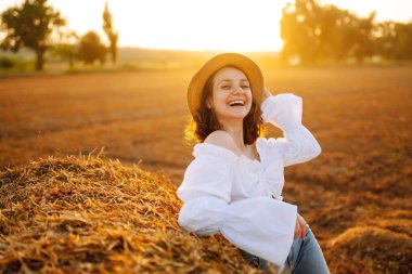 Gün batımında samanlığın yanında mutlu bir kadın. Moda konsepti. Doğa, tatil, rahatlama ve yaşam tarzı. 