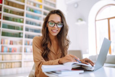 Kablosuz kulaklıklı genç bir kadın dizüstü bilgisayardan arıyor, webcam ile konuşuyor, modern kafede video konferansı yapıyor. Dizüstü bilgisayarda çalışan serbest çalışan biri. İş, çevrimiçi, eğitim kavramı.