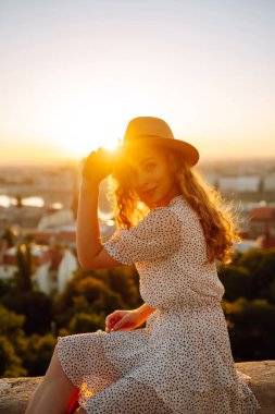 Gün batımında şapkalı genç bir kadının portresi şehrin manzarasının keyfini çıkarıyor. Yaşam tarzı, seyahat, turizm, doğa, aktif yaşam.