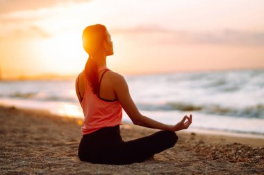 Okyanusun kenarında çıplak ayakla yoga yapan güzel bir kadın. Spor kıyafetli genç bir kadın plajda spor yapıyor. Sakinlik ve denge, sağlıklı bir yaşam tarzı..