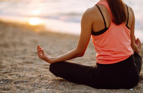 Okyanusun kenarında çıplak ayakla yoga yapan güzel bir kadın. Spor kıyafetli genç bir kadın plajda spor yapıyor. Sakinlik ve denge, sağlıklı bir yaşam tarzı..