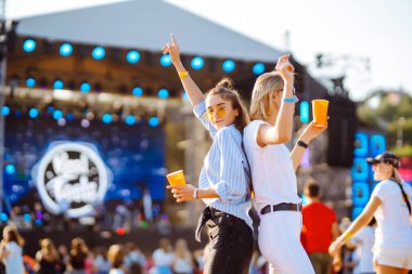 İki genç kadın bira içiyor ve plaj partisinde birlikte eğleniyorlar. Mutlu kız arkadaşlar müzik festivalinde eğleniyor. Yaz tatili, tatil konsepti.