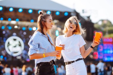 İki genç kadın bira içiyor ve plaj partisinde birlikte eğleniyorlar. Mutlu kız arkadaşlar müzik festivalinde eğleniyor. Yaz tatili, tatil konsepti.