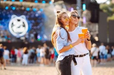 İki genç kadın bira içiyor ve plaj partisinde birlikte eğleniyorlar. Mutlu kız arkadaşlar müzik festivalinde eğleniyor. Yaz tatili, tatil konsepti.
