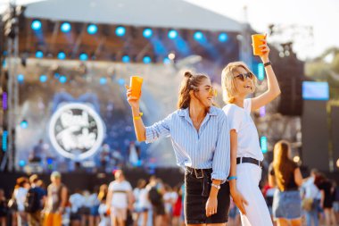 İki genç kadın bira içiyor ve plaj partisinde birlikte eğleniyorlar. Mutlu kız arkadaşlar müzik festivalinde eğleniyor. Yaz tatili, tatil konsepti.