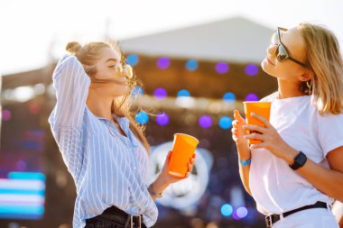 İki genç kadın bira içiyor ve plaj partisinde birlikte eğleniyorlar. Mutlu kız arkadaşlar müzik festivalinde eğleniyor. Yaz tatili, tatil konsepti.