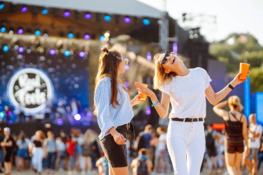 İki genç kadın bira içiyor ve plaj partisinde birlikte eğleniyorlar. Mutlu kız arkadaşlar müzik festivalinde eğleniyor. Yaz tatili, tatil konsepti.