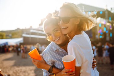 İki genç kadın bira içiyor ve plaj partisinde birlikte eğleniyorlar. Mutlu kız arkadaşlar müzik festivalinde eğleniyor. Yaz tatili, tatil konsepti.
