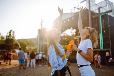 İki genç kadın bira içiyor ve plaj partisinde birlikte eğleniyorlar. Mutlu kız arkadaşlar müzik festivalinde eğleniyor. Yaz tatili, tatil konsepti.