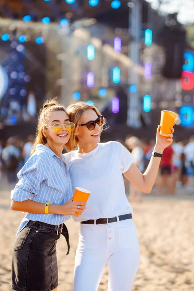 İki genç kadın bira içiyor ve plaj partisinde birlikte eğleniyorlar. Mutlu kız arkadaşlar müzik festivalinde eğleniyor. Yaz tatili, tatil konsepti.
