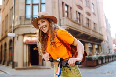 Yazın sokakta elektrikli scooter süren genç ve güzel bir kadın. Aktif hayat. Ekolojik ulaşım kavramı.