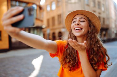 Selfie time. Young woman olding mobile phone taking selfie photo using smartphone camera. Beautiful girl walks through the streets  and takes pictures of some sights .Lifestyle, travel, tourism.