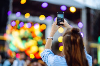 Using a smartphone in a public event, live music festival. Holding a mobile phone in hands and shooting photo or video content. Youth, party, vacation concept.