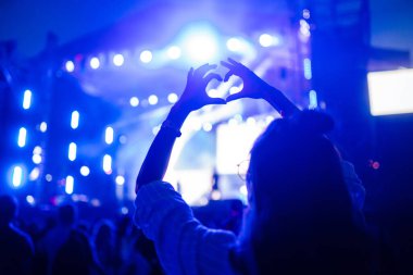 Heart shaped hands at concert, loving the artist and the festival. Music concert with lights and silhouette of people enjoying the concert. clipart