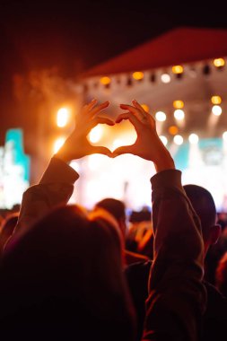 Heart shaped hands at concert, loving the artist and the festival. Music concert with lights and silhouette of people enjoying the concert. clipart