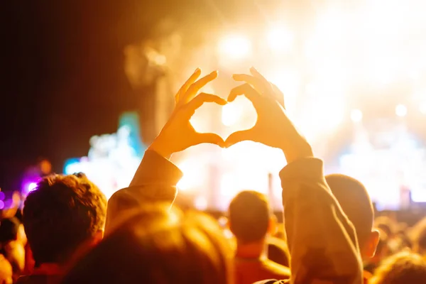 Heart shaped hands at concert, loving the artist and the festival. Music concert with lights and silhouette of people enjoying the concert.