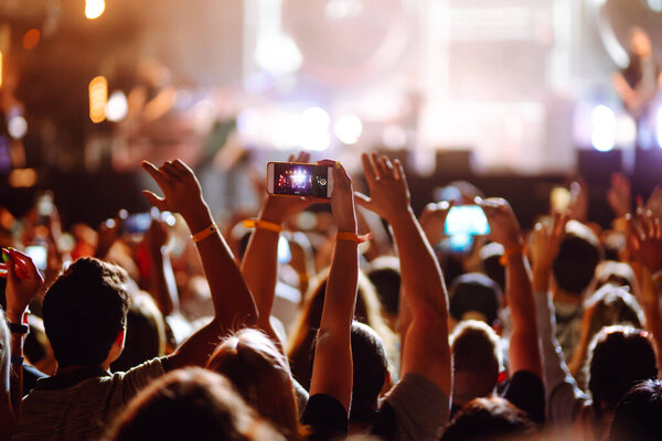 Using a smartphone in a public event, live music festival. Holding a mobile phone in hands and shooting photo or video content. Youth, party, vacation concept.