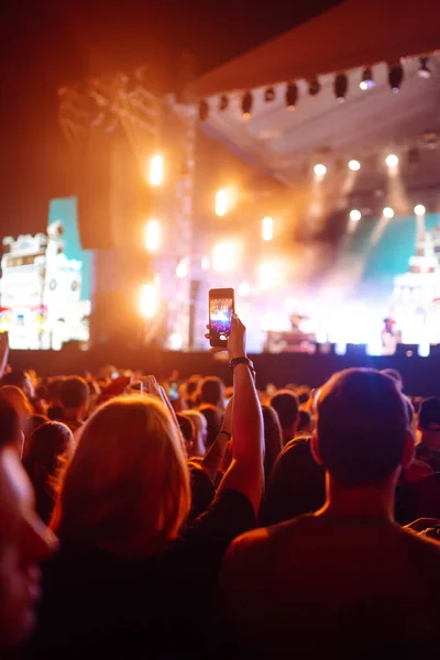 Using a smartphone in a public event, live music festival. Holding a mobile phone in hands and shooting photo or video content. Youth, party, vacation concept.