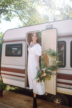 Karavanın yanında güzel, şık bir gelin. Kamp sezonu. Evlilikten. Mutlu yeni evli kadın.