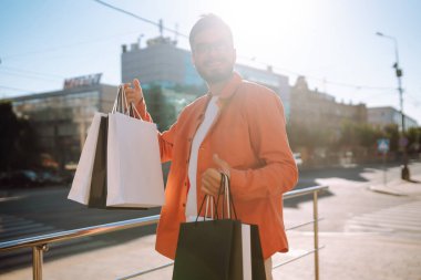 Alışveriş torbalarıyla sokakta yürüyen gülümseyen adam. Satın almalar, Kara Cuma, indirimler, satış konsepti. 