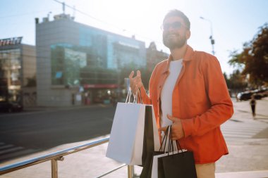 Alışveriş torbalarıyla sokakta yürüyen gülümseyen adam. Satın almalar, Kara Cuma, indirimler, satış konsepti. 