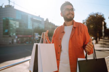 Alışveriş torbalarıyla sokakta yürüyen gülümseyen adam. Satın almalar, Kara Cuma, indirimler, satış konsepti. 