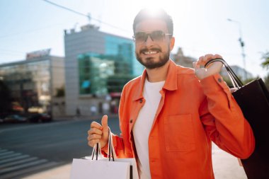 Alışveriş torbalarıyla sokakta yürüyen gülümseyen adam. Satın almalar, Kara Cuma, indirimler, satış konsepti. 